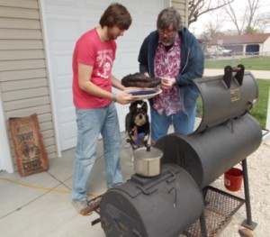 Rick holds the brisket while Rich tries to put it back on the pit.